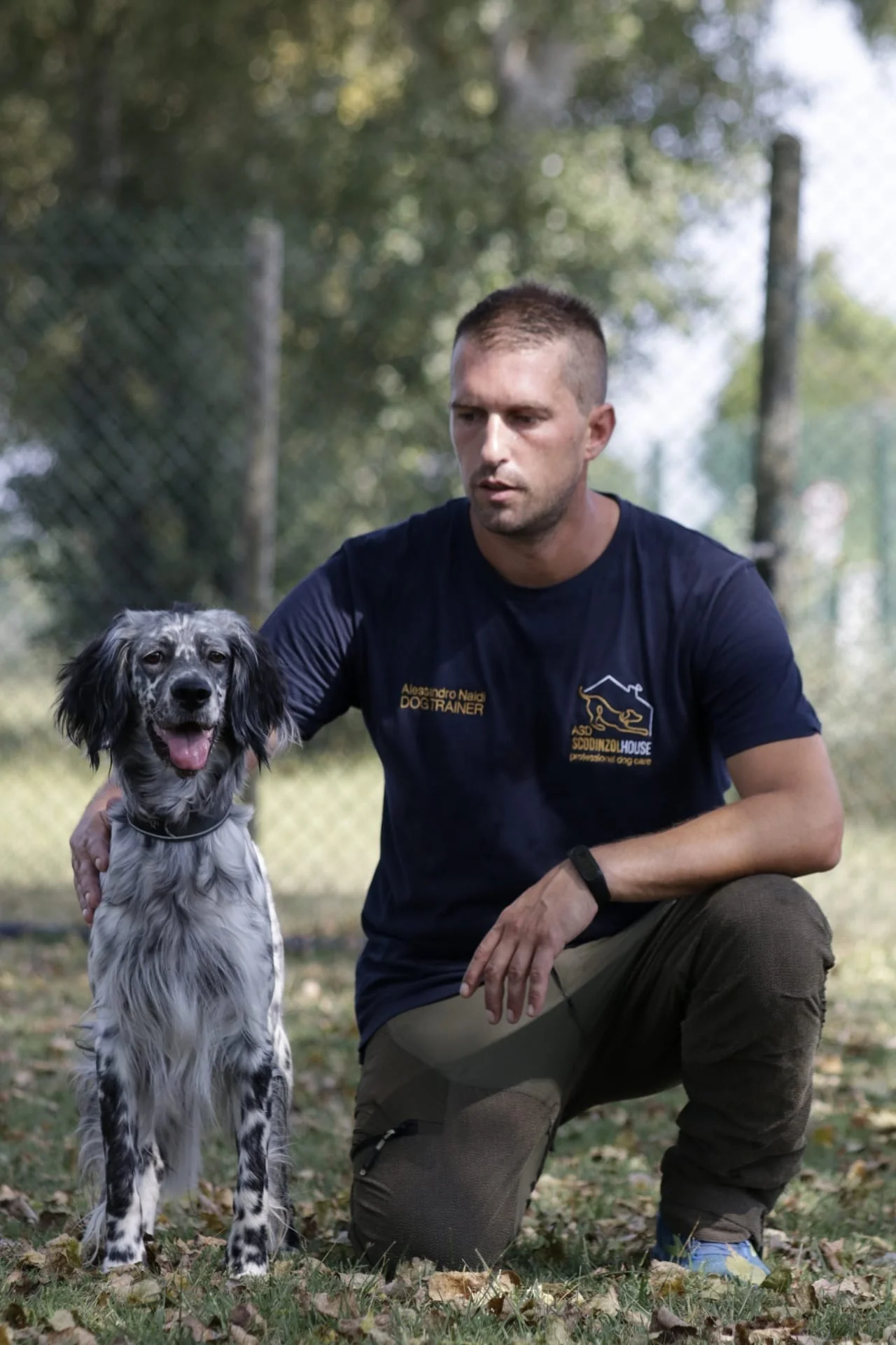 Educatore di ScodinzolHouse inginocchiato accanto a un setter inglese seduto sul prato