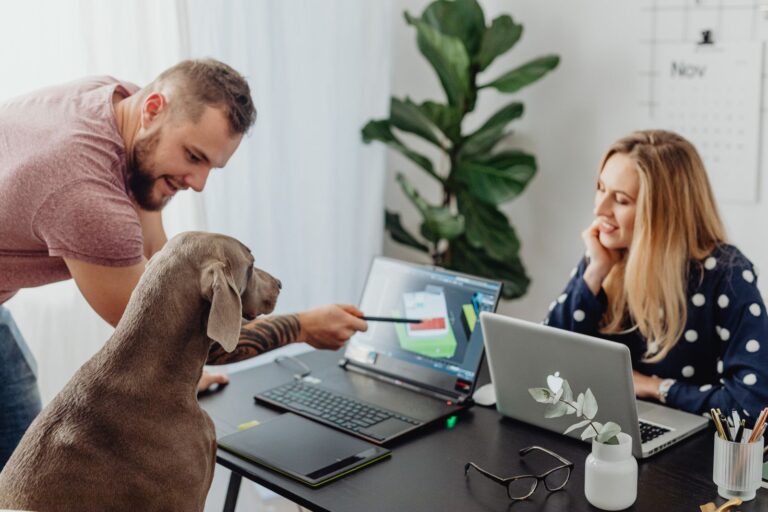 Due colleghi lavorano alla scrivania con il cane accanto a loro, in ufficio